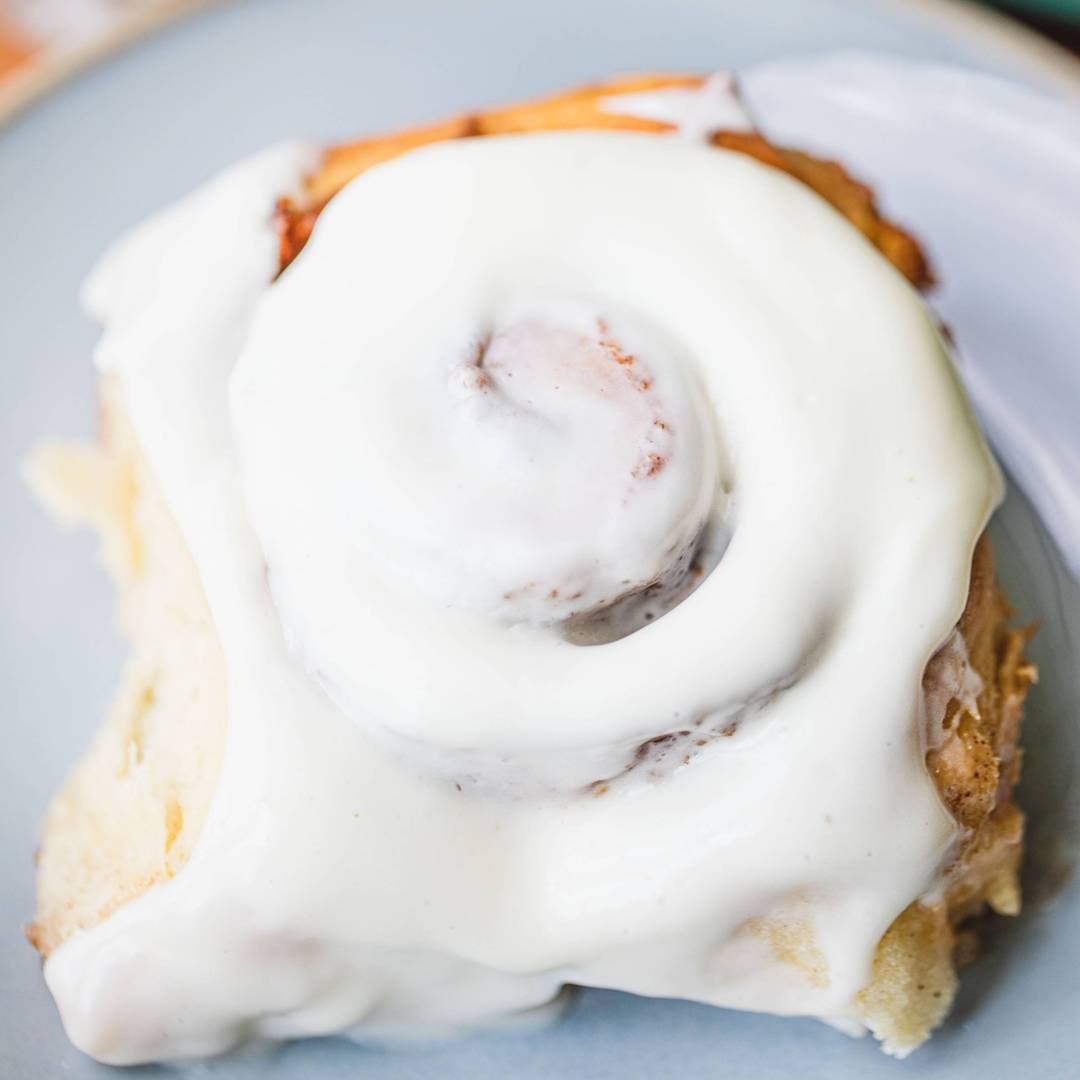 big gooey cinnamon roll sits on plate covered in icing