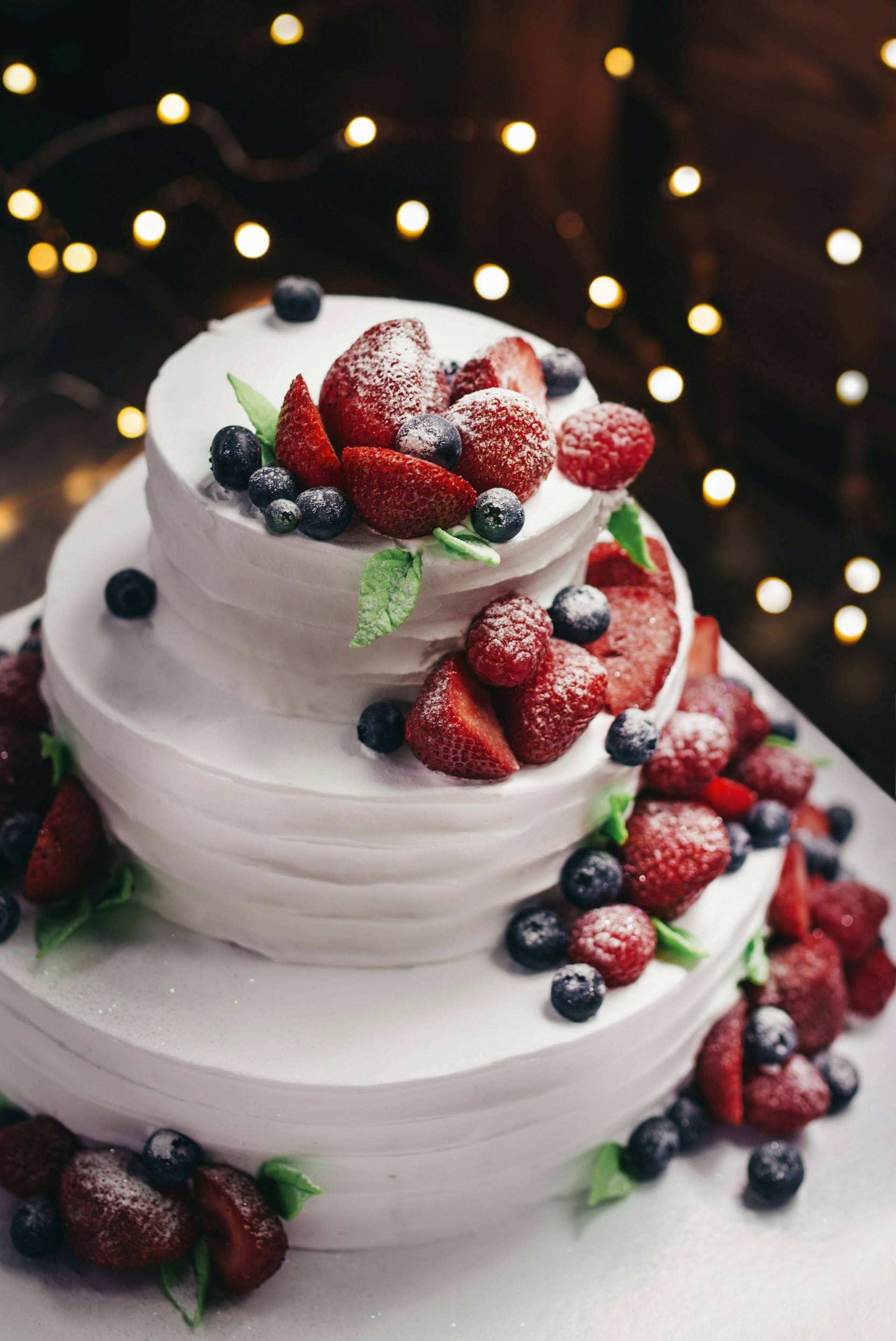 A celebration cake in three layers with fresh berries cascading down its side.