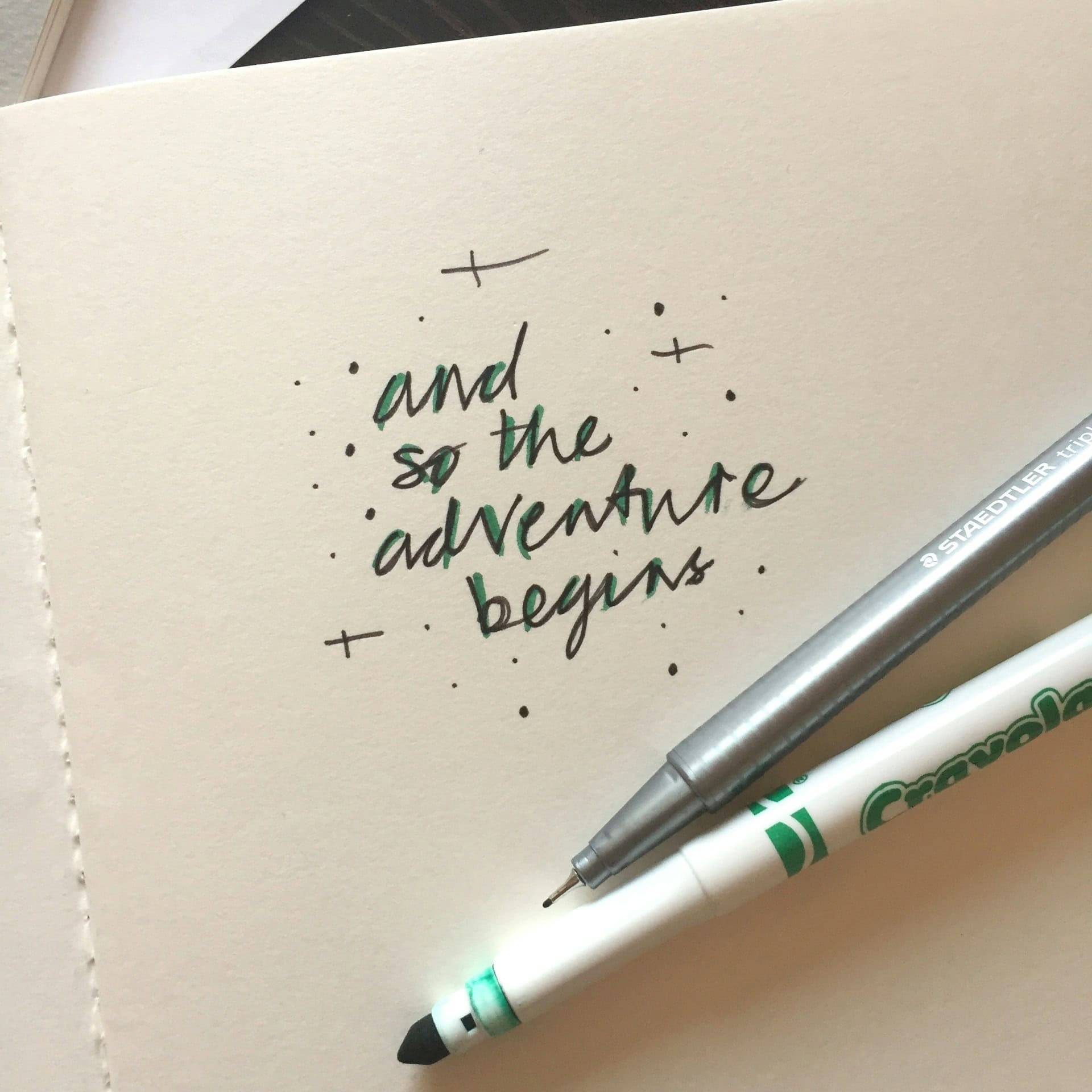 A piece of paper with a green pen that's written 'and so the adventure begins.'