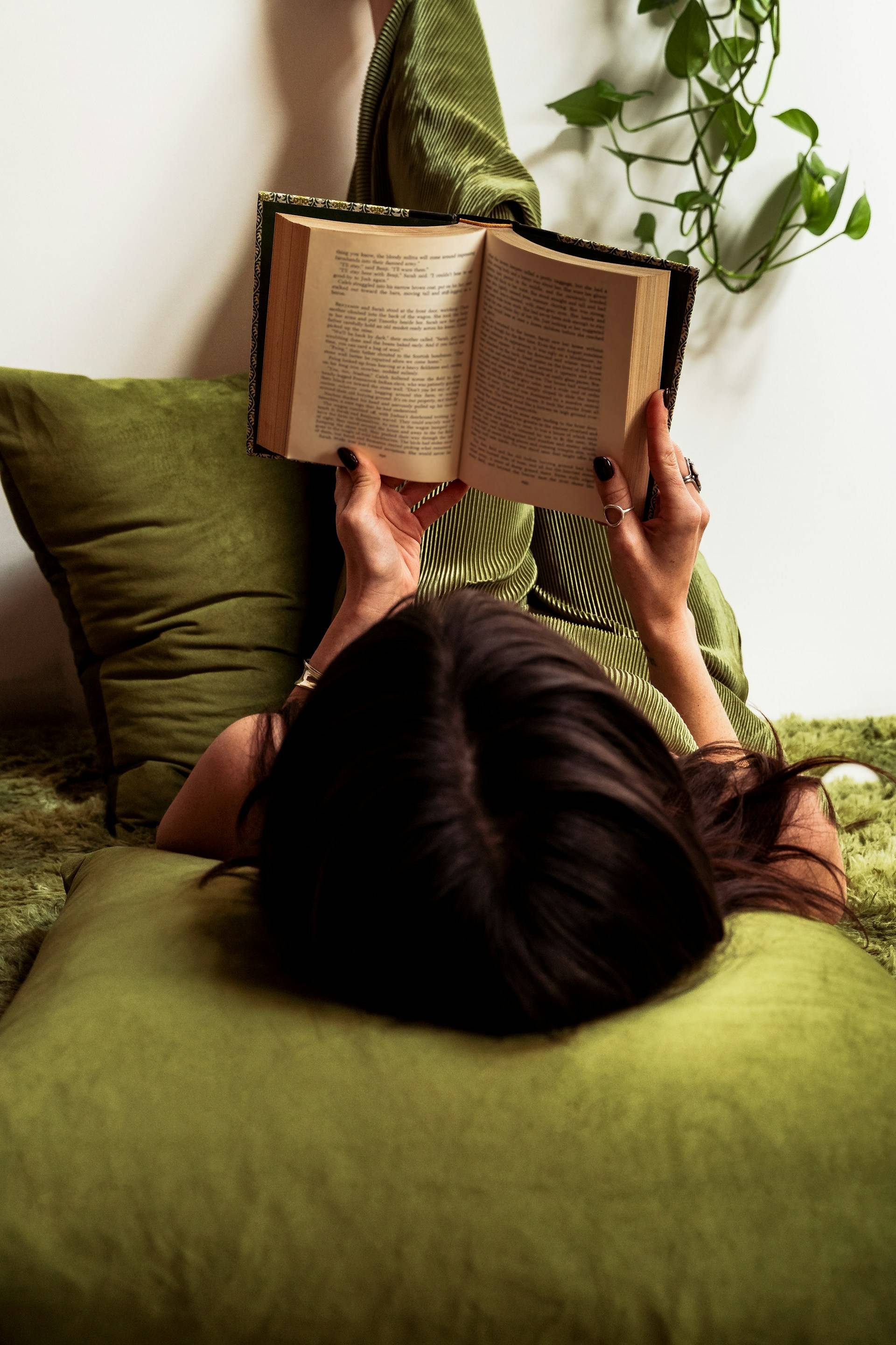 A woman dressed in green reading a book amidst a green backdrop.