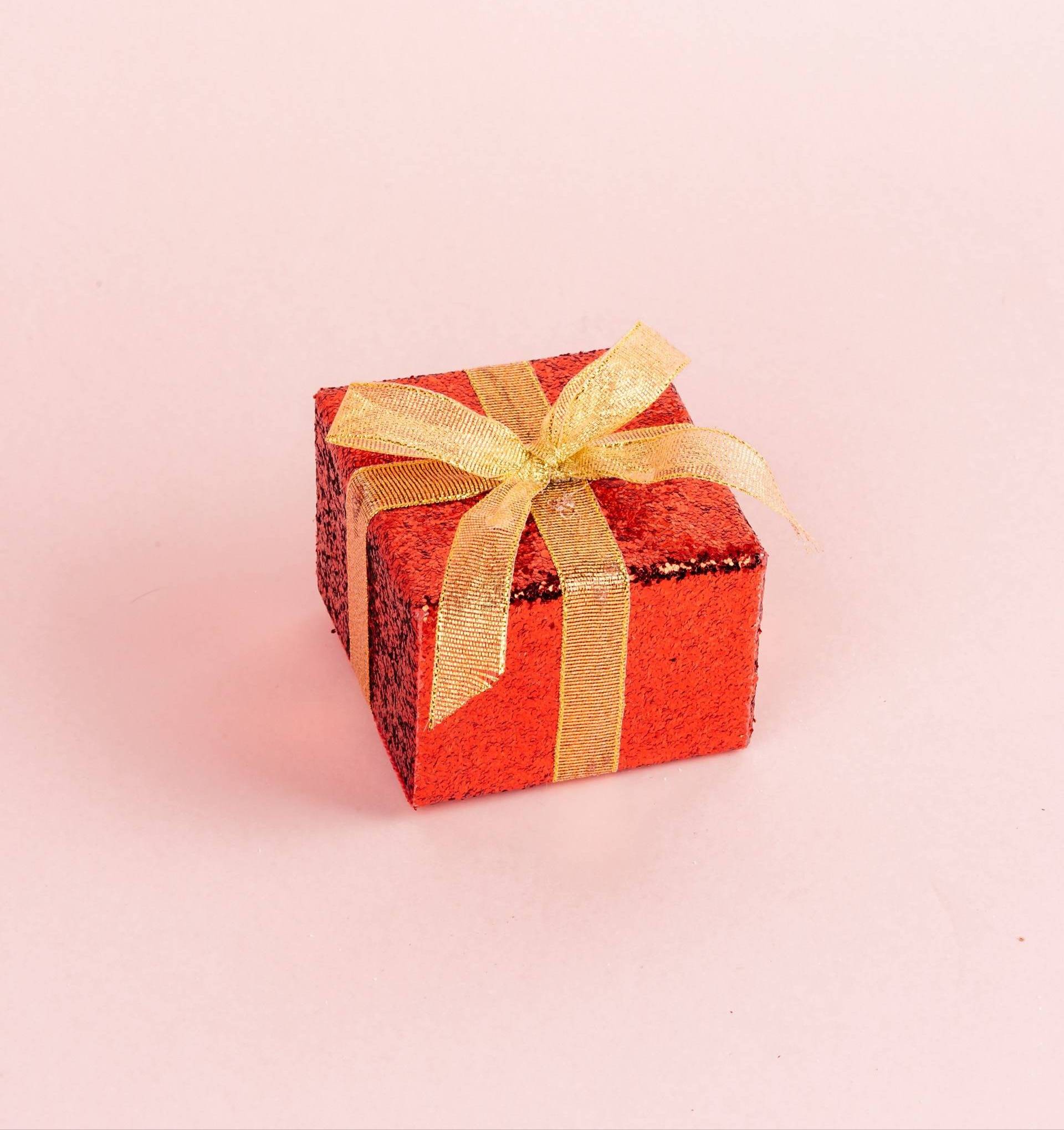 A wrapped gift in shiny red paper tied with a gold bow.