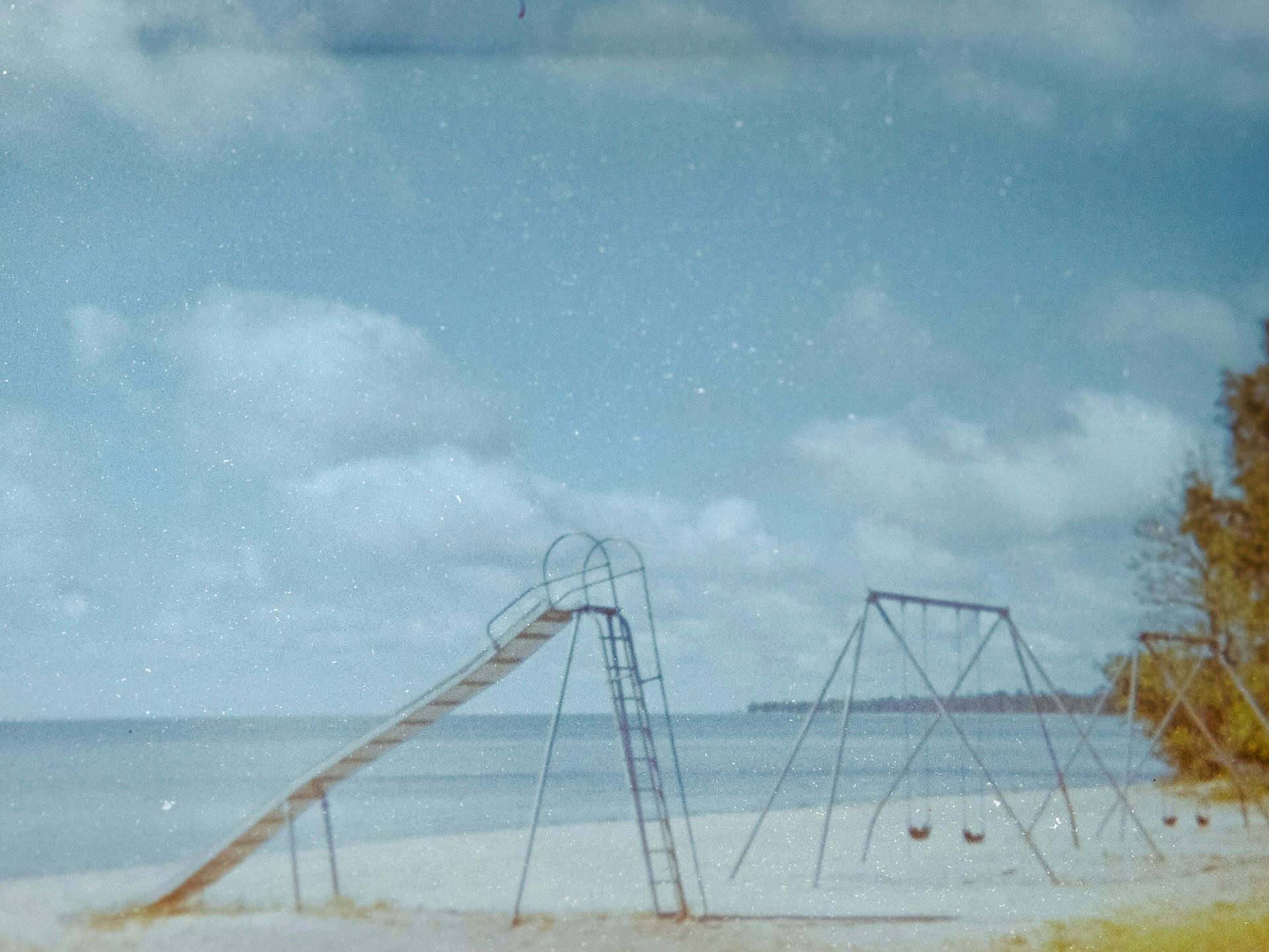 An empty swing set and slide along the shore of a lake in fall.