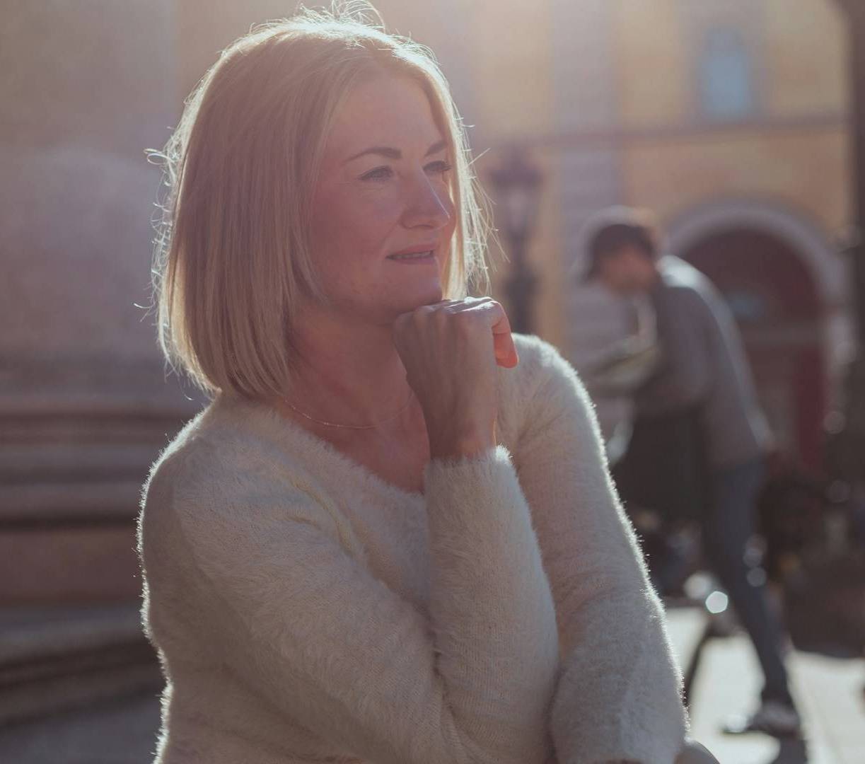 A woman standing in a white sweater, contemplating being brave in midlife.