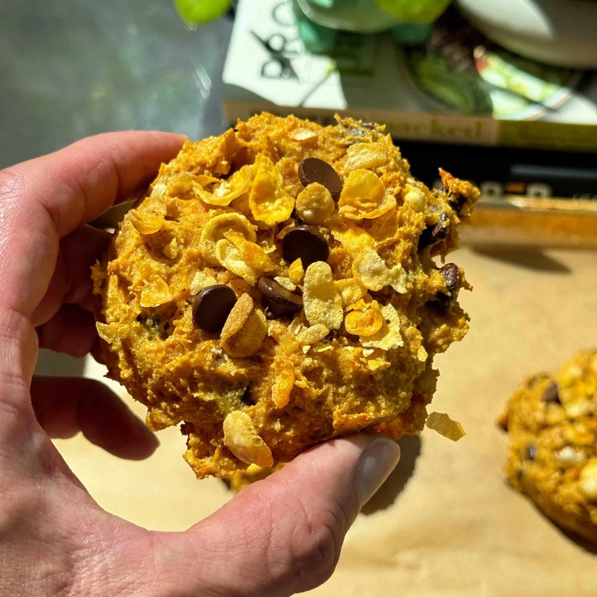 A hand holding a pumpkin corn flake protein breakfast cookie