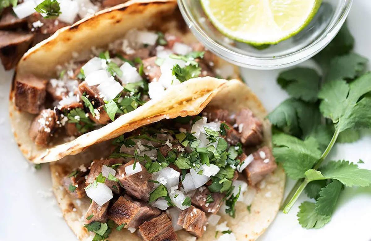 image of delicious stree tacos on a white counter with cilantro and lime hugging the outside perimeter of the frame