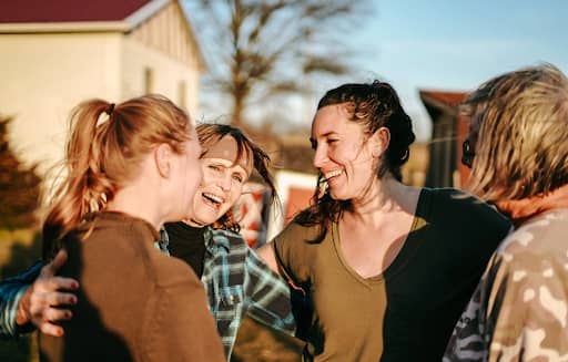 Women sharing a joyful group embrace at The Wild Unknown retreat, laughing together outdoors in the golden evening light, celebrating connection, belonging, and community.
