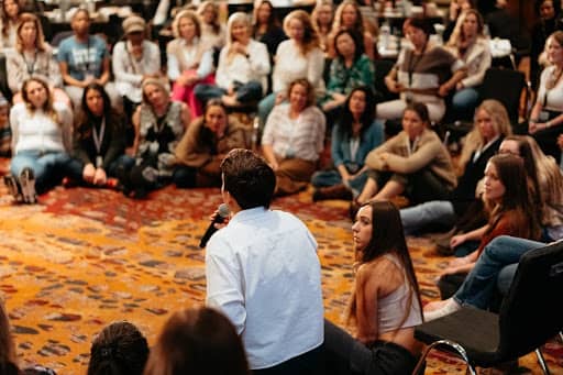 Tarzan Kay leading a group singing experience for 200 attendees at Kate Northrup’s Relaxed Money Live event, bringing participants together in a large circle for community building, connection, and transformational learning.