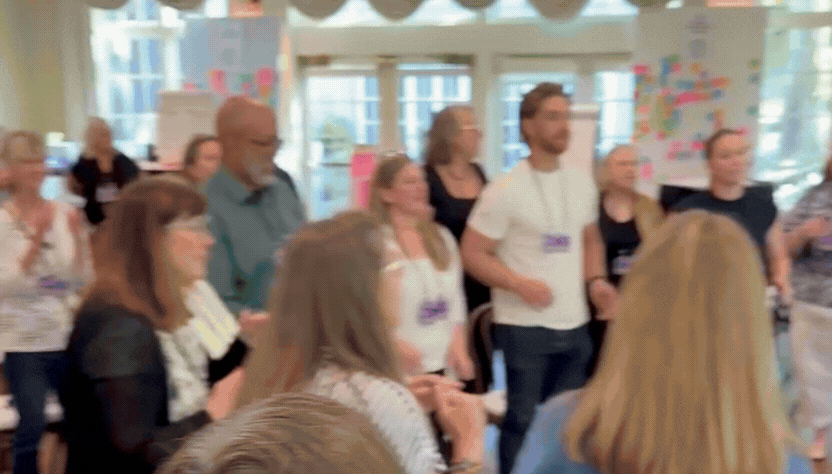 Animated GIF of Tarzan Kay leading a community song circle with joy and enthusiasm, inviting participants into a shared experience of music, connection, creativity, and belonging through collective singing.