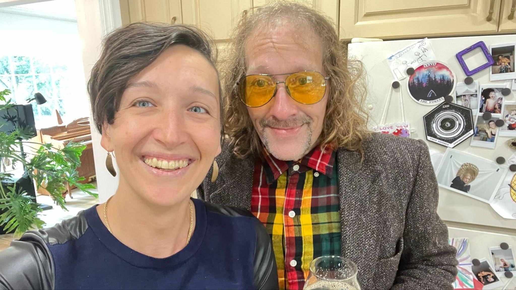 A selfie of Tarzan and her brother Quentin, both smiling at the camera. Tarzan wears a navy blue top with leather sleeves, small earrings, and her short brown hair sweeping down one side of her face; she has a wide, open smile and blue eyes. Quentin wears