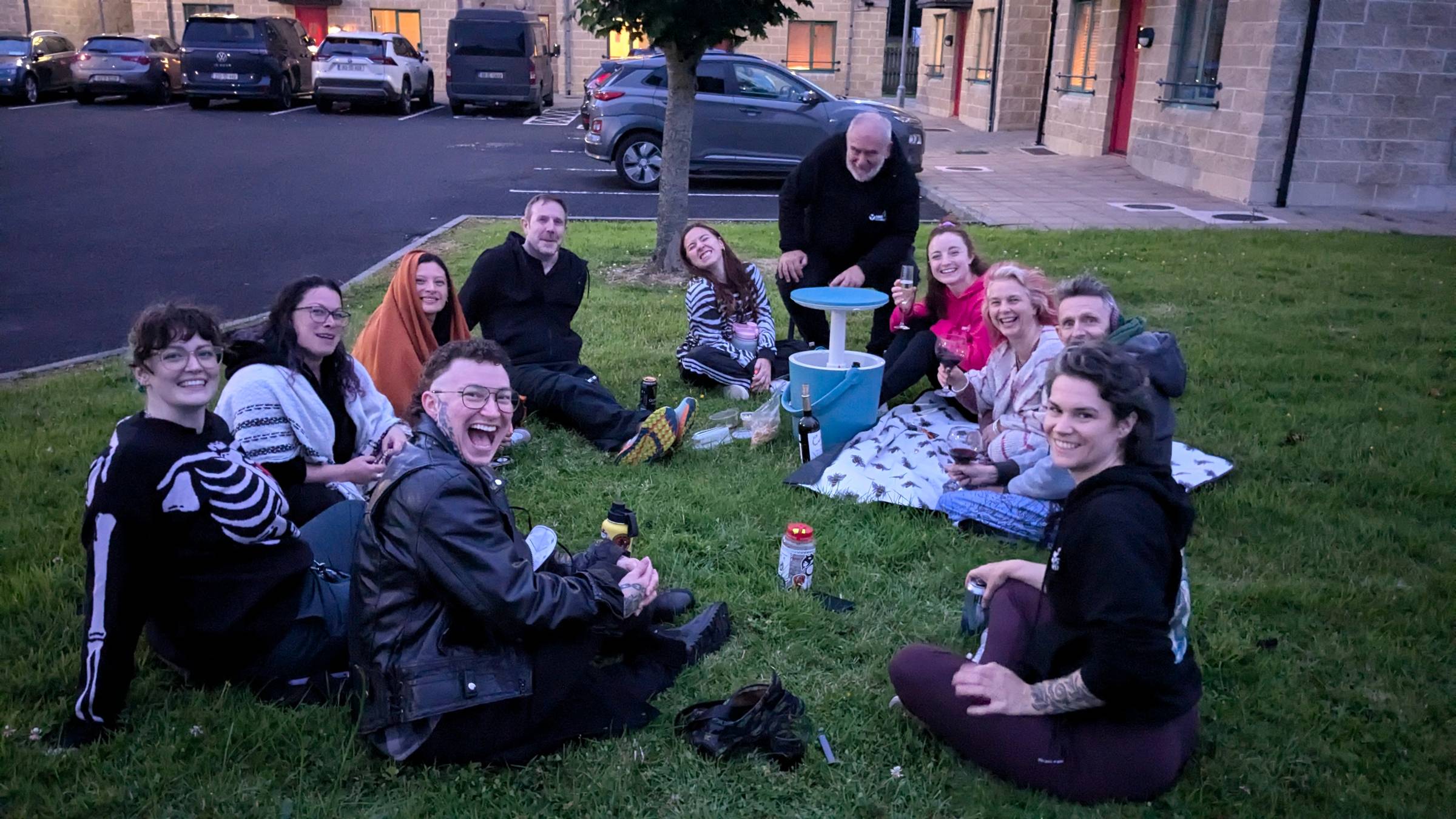 a candid image of a twilight picnic with 11 friends sitting on the grass smiling at the camera