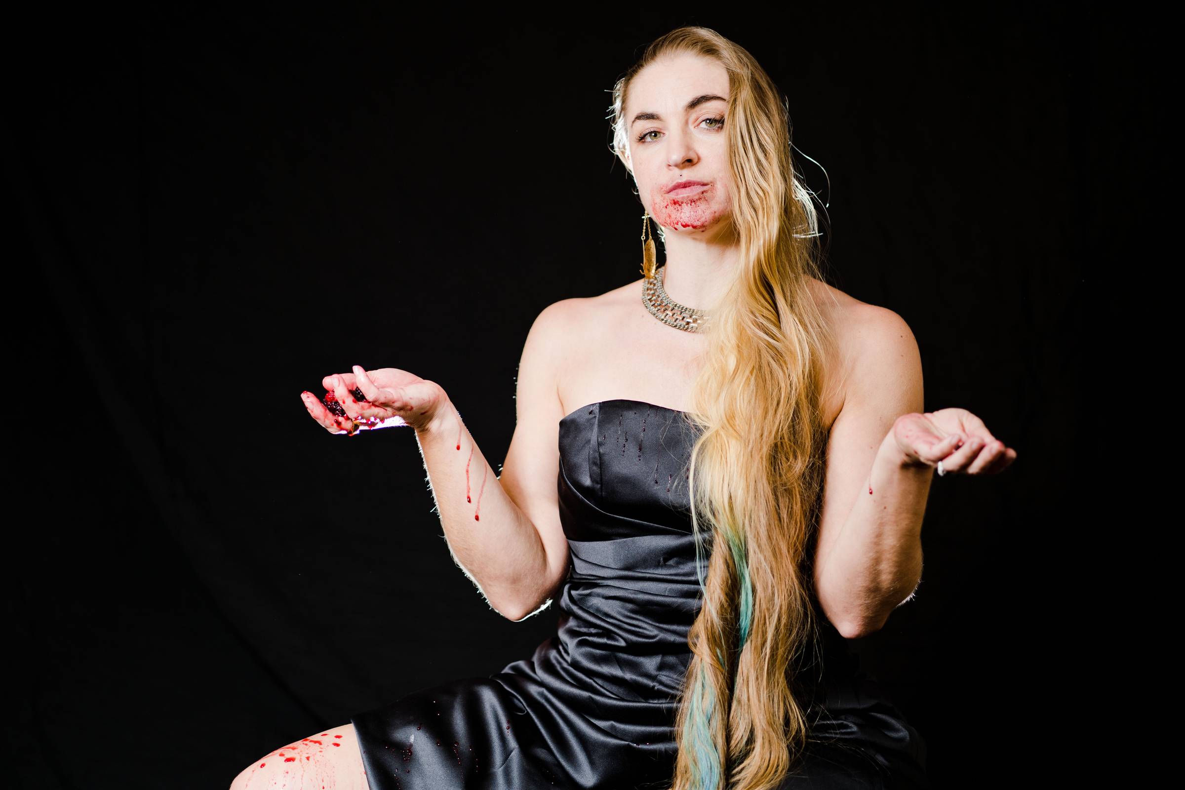 a portrait of a white woman on a black background.  She is wearing a black ballgown and long blonde hair.  Her face is smeared with berry juice.  The juice drips down her leg as well, and she holds crushed berries in her hand