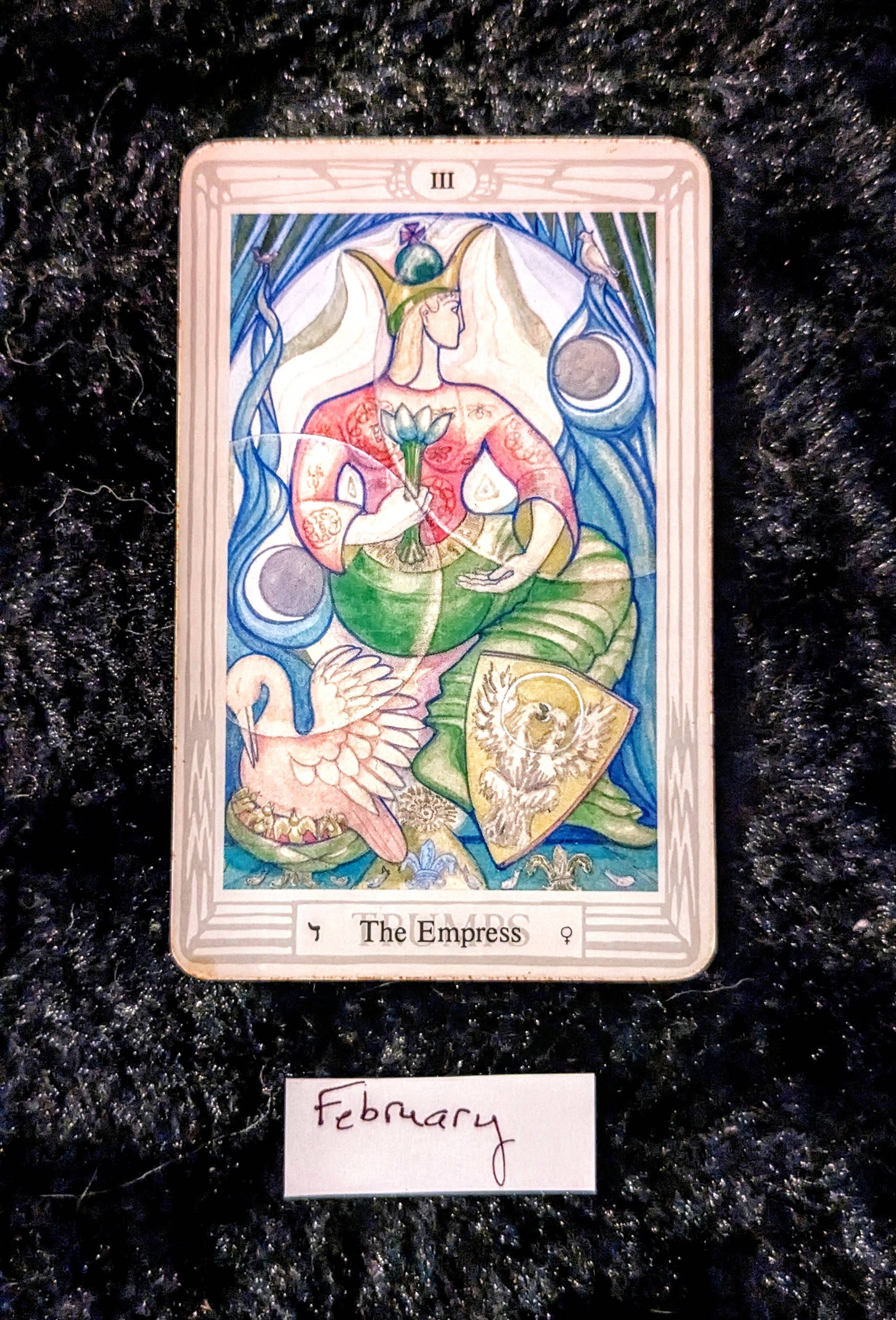 an image of the empress card in the Thoth tarot deck, on a black fur background.  the card depicts a matronly figure in muted pinks and greens, with a nesting bird and a shield at her feet.  She is holding a lotus blossom.