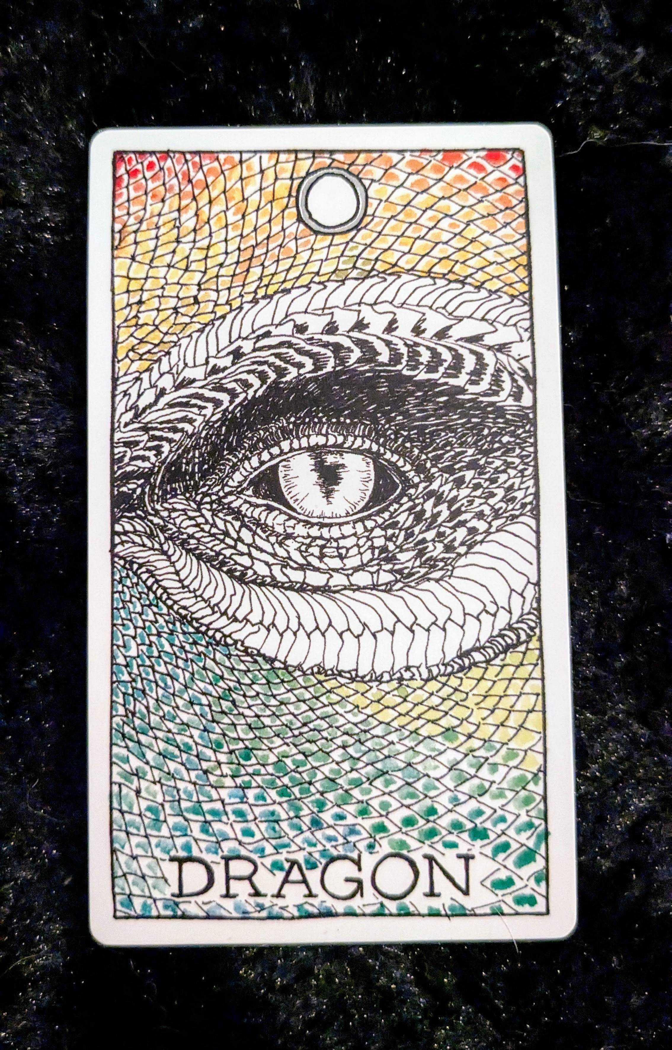 an image of the dragon card from the wild unknown deck on a black fur background.  the card features an illustration of a dragon's eye up close, with rainbow colored scales