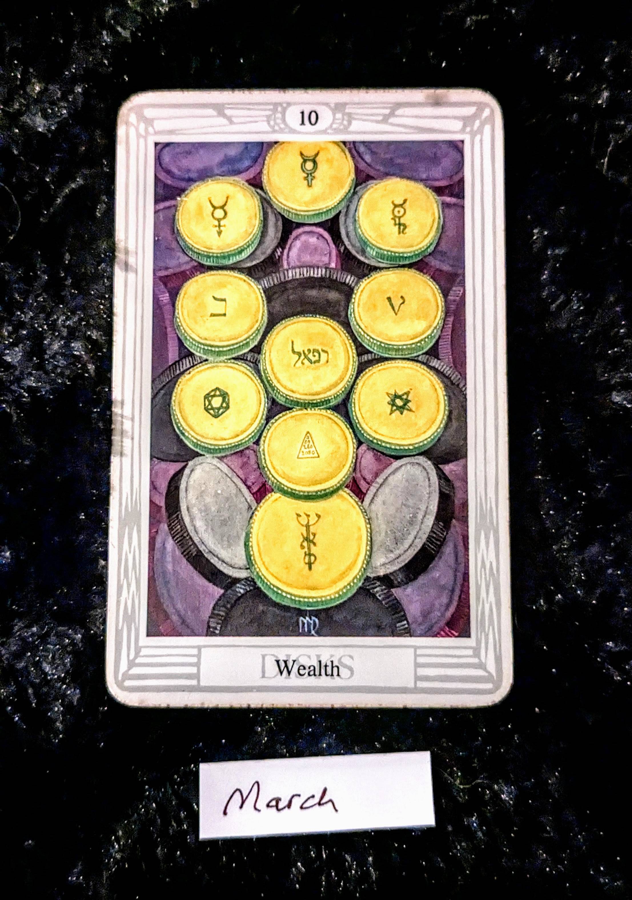 a photo of the 10 of disks of the Thoth tarot deck, picturing 10 gold coins.  The word "Wealth" is printed at the bottom of the card.  The card rests on a black fur background, and a handwritten slip of paper reads "March" underneath it.