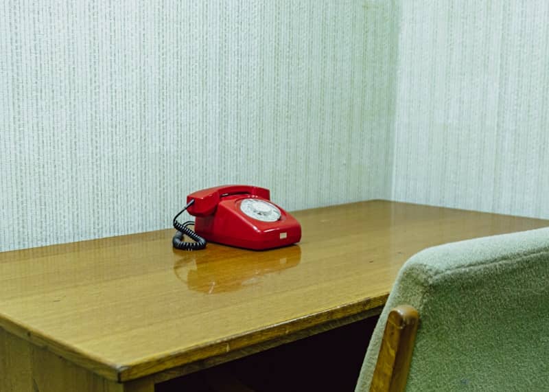 A red rotary telephone on a wooden desk.
