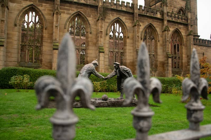 Two statues shake hands in front of ruined building