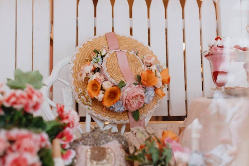 A floral straw hat hangs on a white fence.