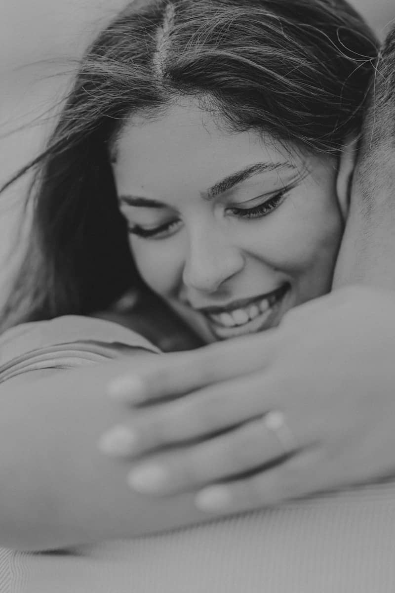 A smiling woman with her eyes closed, embraced by arms