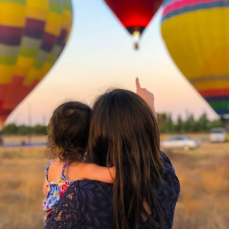 woman carrying toddler point at hot air balloon