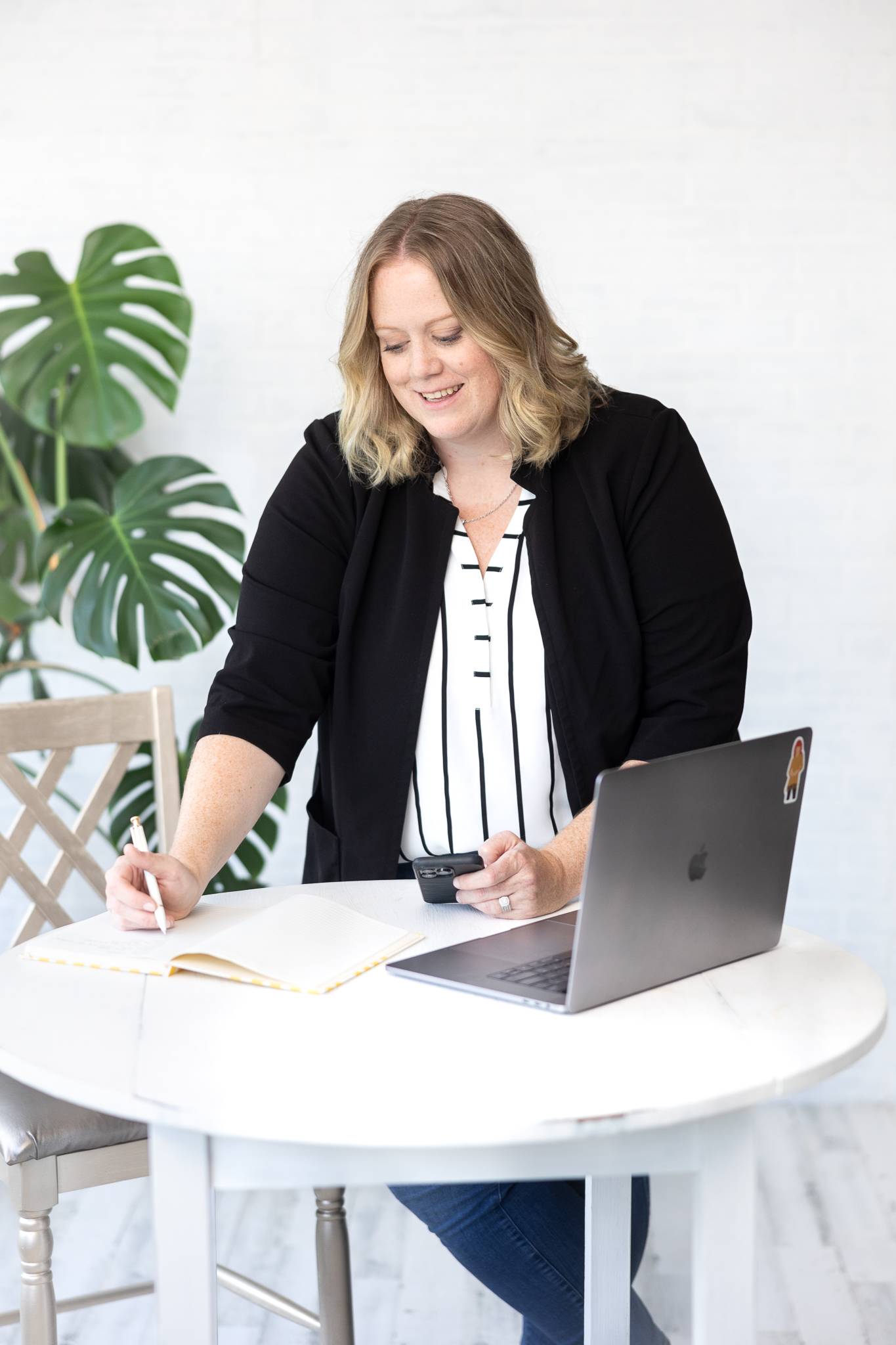 Jen writing in a notebook at a desk with a laptop and coffee