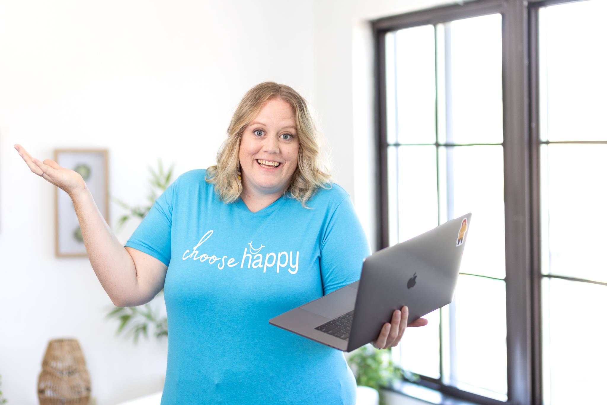 Jen holding a laptop and smiling, wearing a teal "choose happy" t-shirt