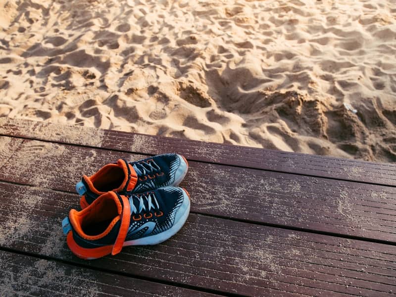 Shoes are resting on the wooden deck near sand.