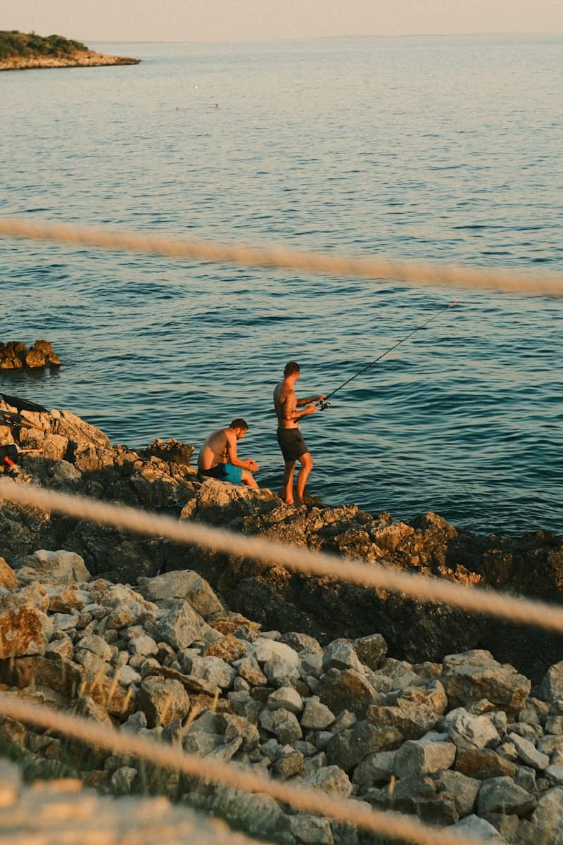 Two men fish on a rocky coastline.