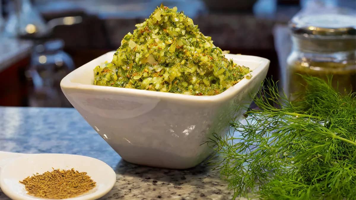 Square white bowl of cucumber dill relish with dill seeds and dill sprigs on the side.