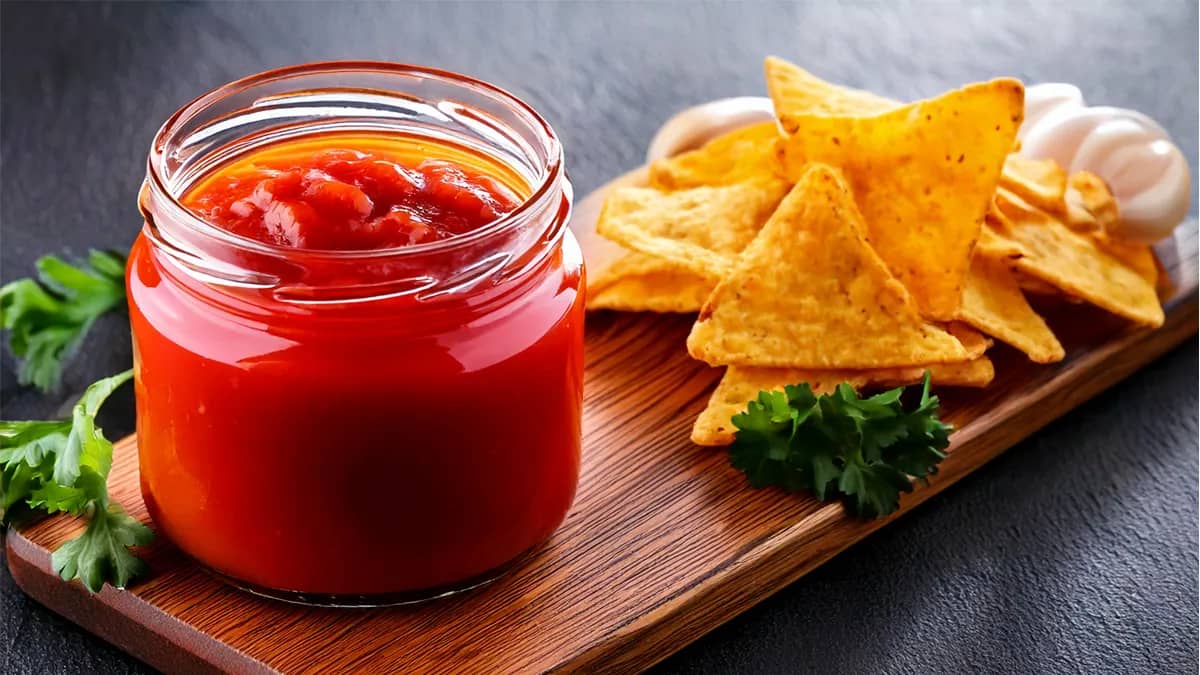 Homemade taco sauce in a glass jar with tortilla chips on the side.
