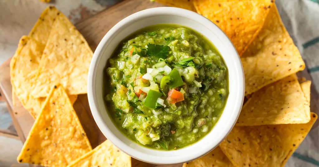 tomatillo salsa in a white bowl surrounded by tortilla chips