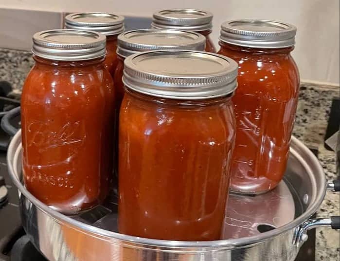 Quart jars of tomato sauce in a steam canner on the stove.
