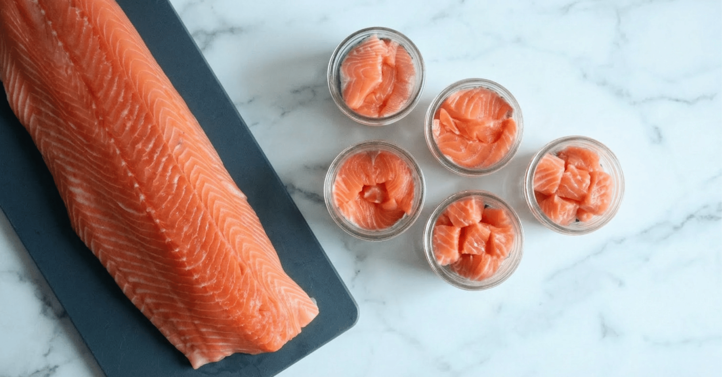 Salmon filet on a dark cutting board with five mason jars full of sliced salmon sitting on a marble countertop.