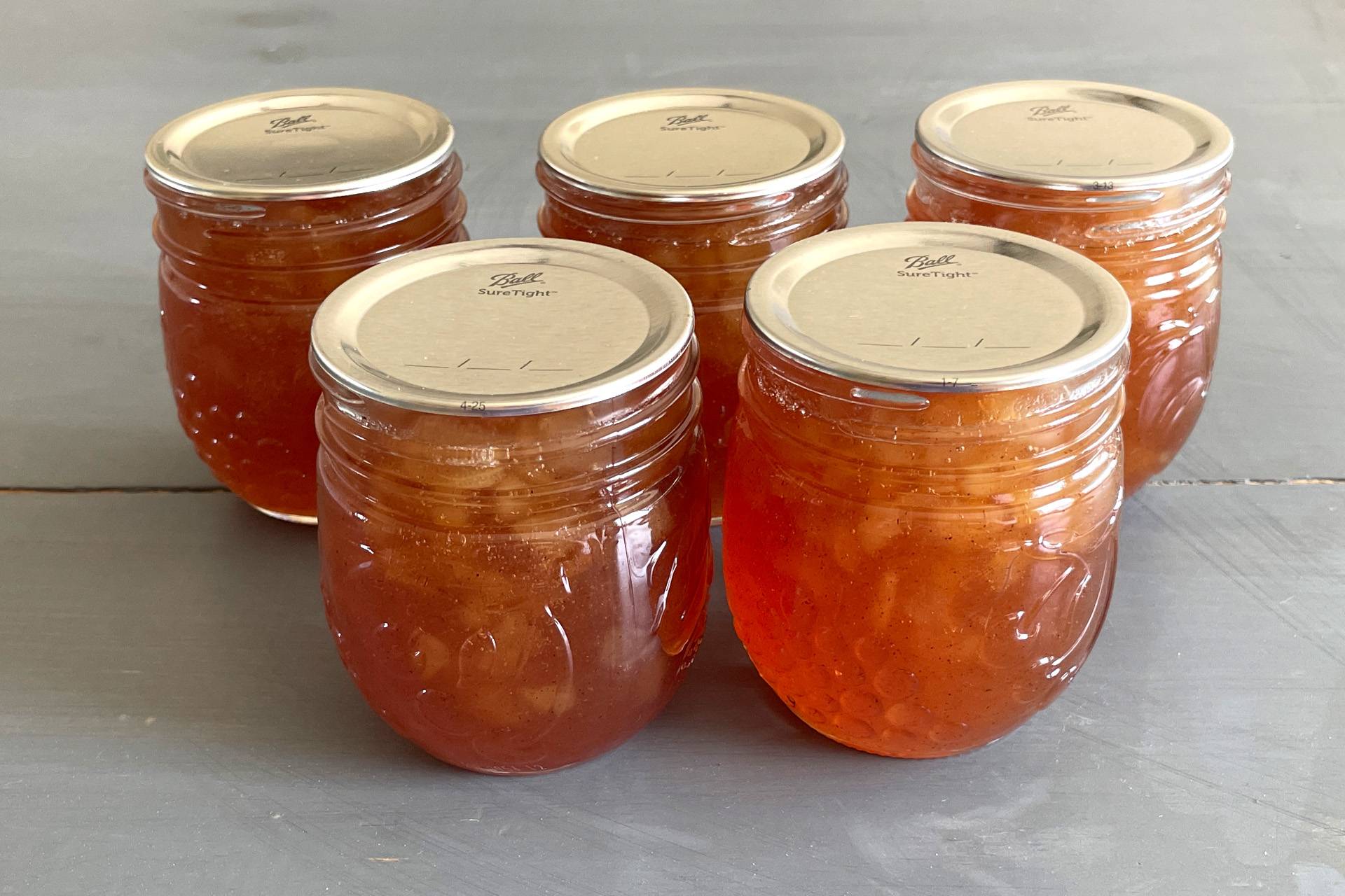 Five mason jars of Cinnamon Pear Jam on a gray surface.