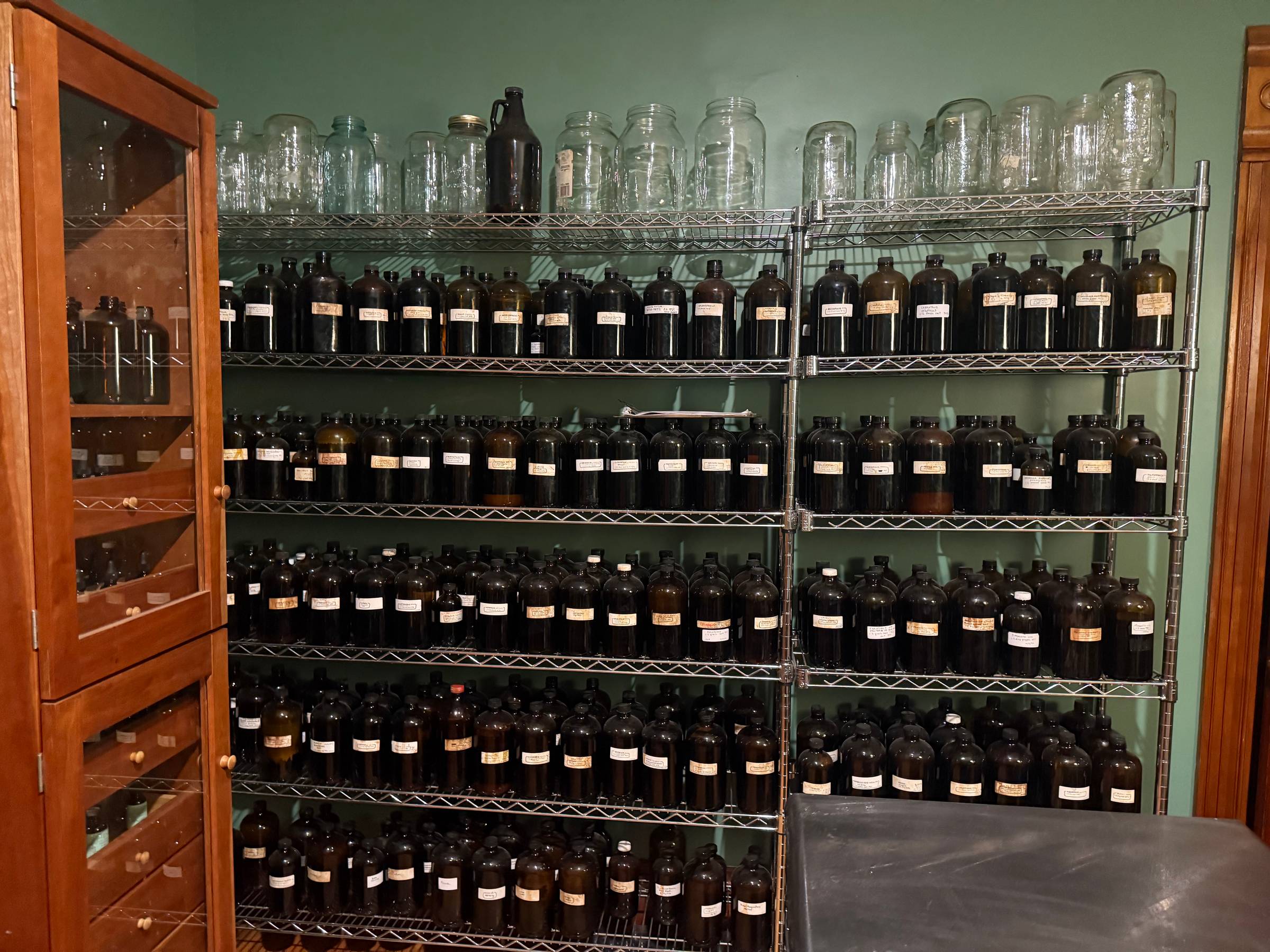 Many large tincture bottles on shelving, a well stocked apothecary.