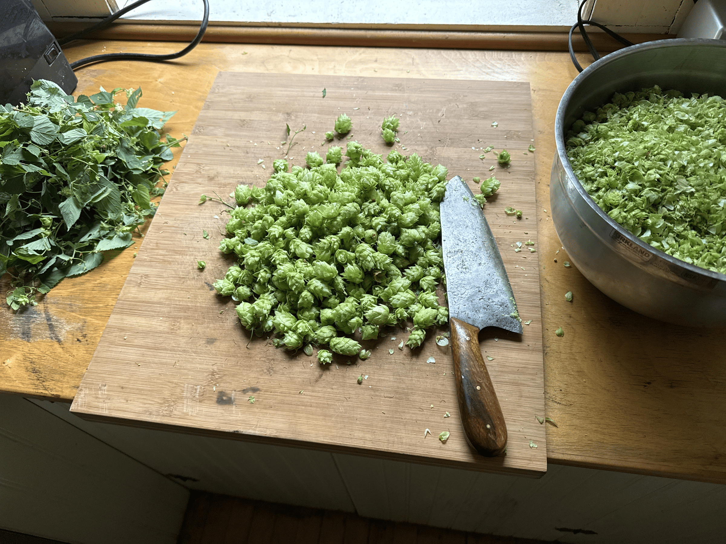 Hops on a cutting board with knife and a bowl of chopped hops