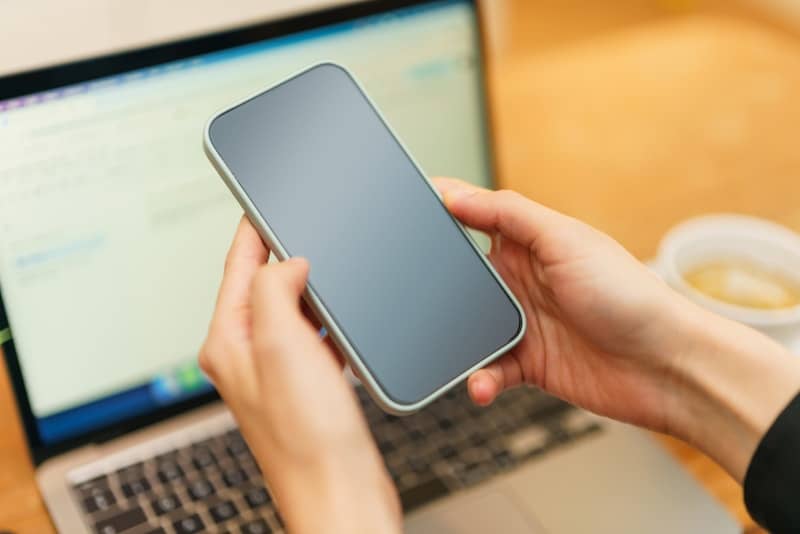 A person holding a cell phone in front of a laptop