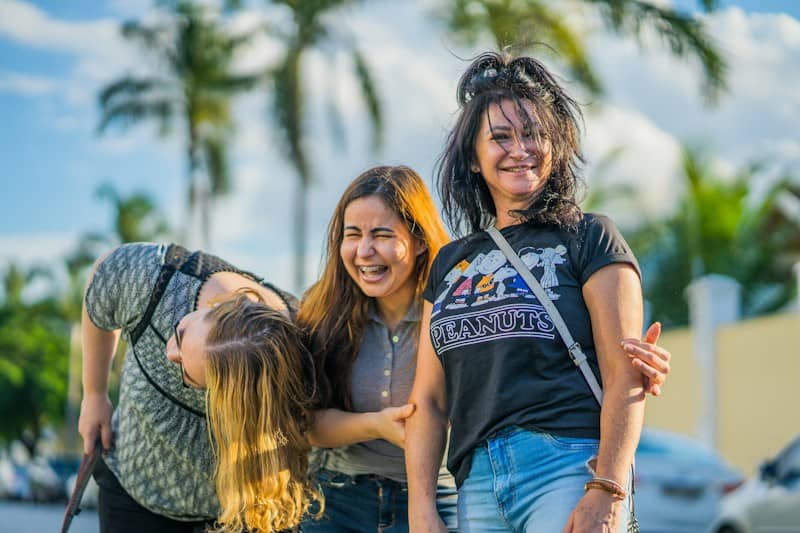 Three women laughing together outdoors with palm trees in the background