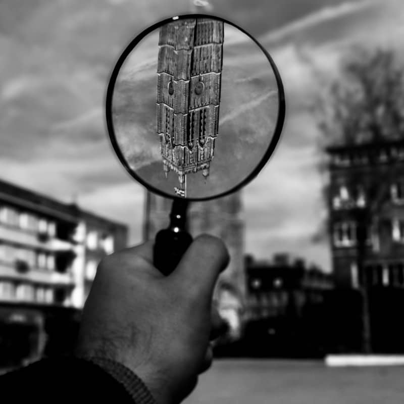 A hand holding a magnifying glass focuses on a building.