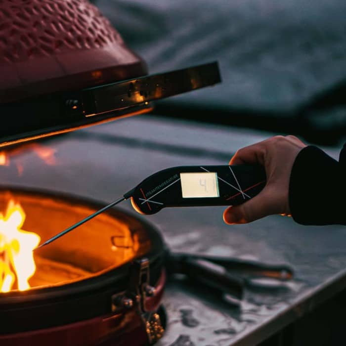 Un thermomètre de cuisson devant un barbecue rouge de type kamado.