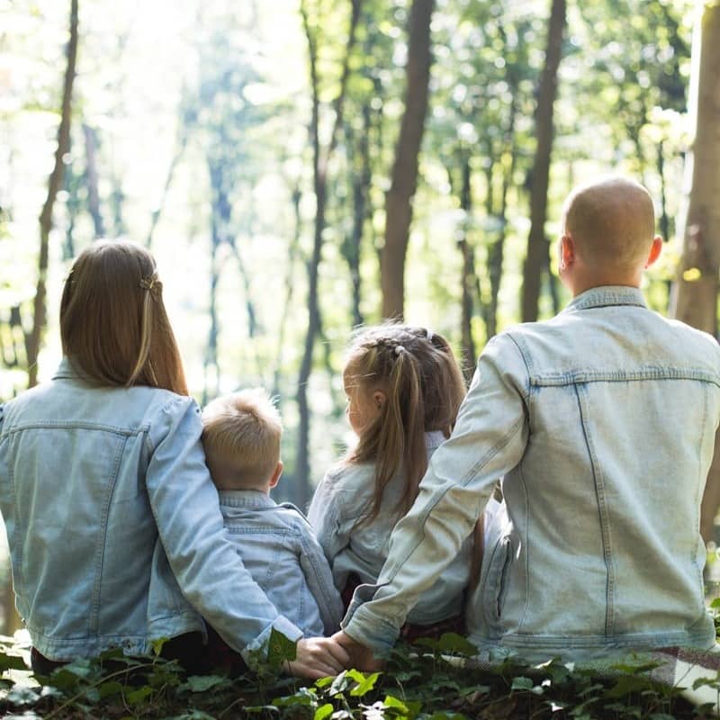 man and woman holding hands together with boy and girl looking at green trees during day