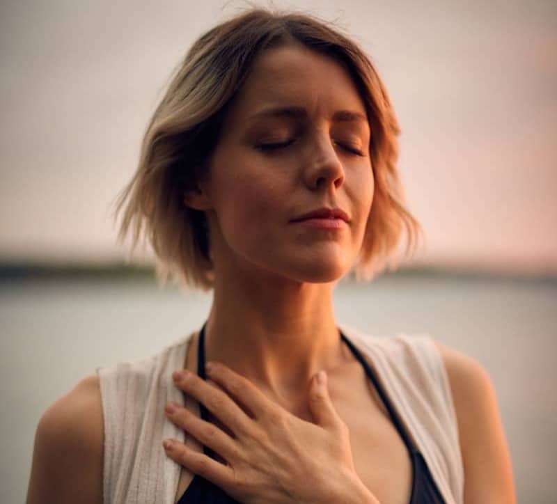 woman in white vest and black bikini with hand on chest