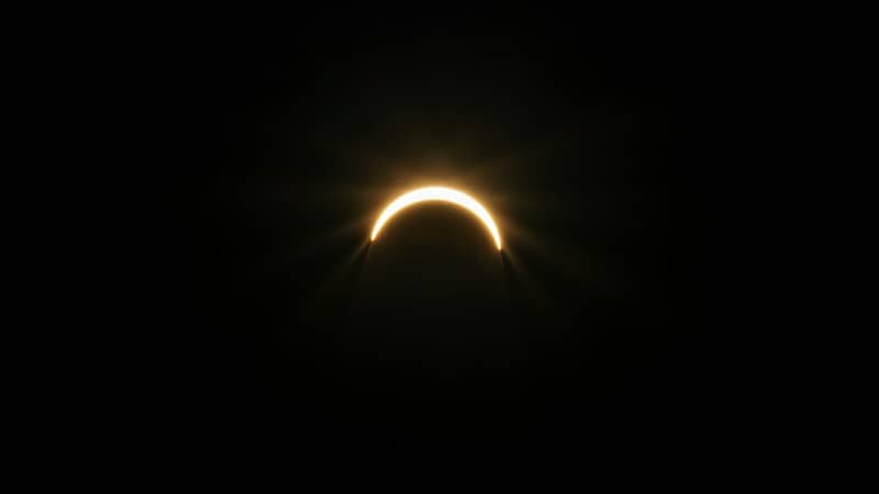 A bright crescent of light from a solar eclipse against a black sky.