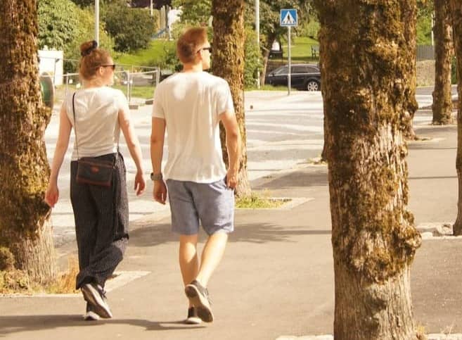 man in white t-shirt walking on sidewalk during daytime