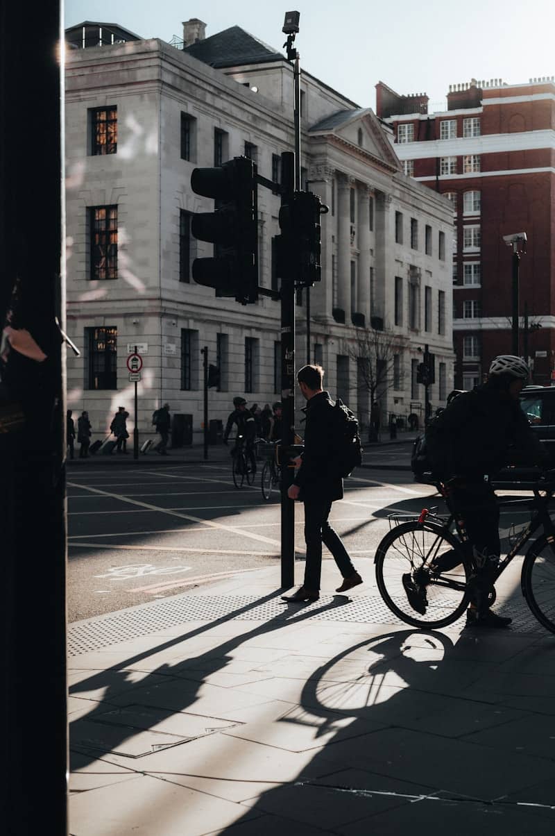 Pedestrians and cyclist at a city intersection with long shadows.