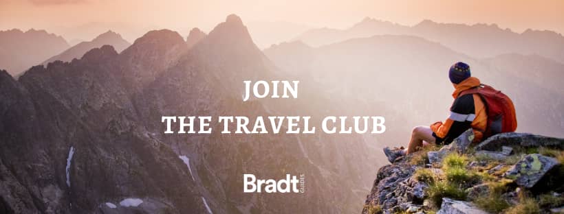 Man sits on the edge of a cliff at sunset for a banner advertising Bradt's Travel Club