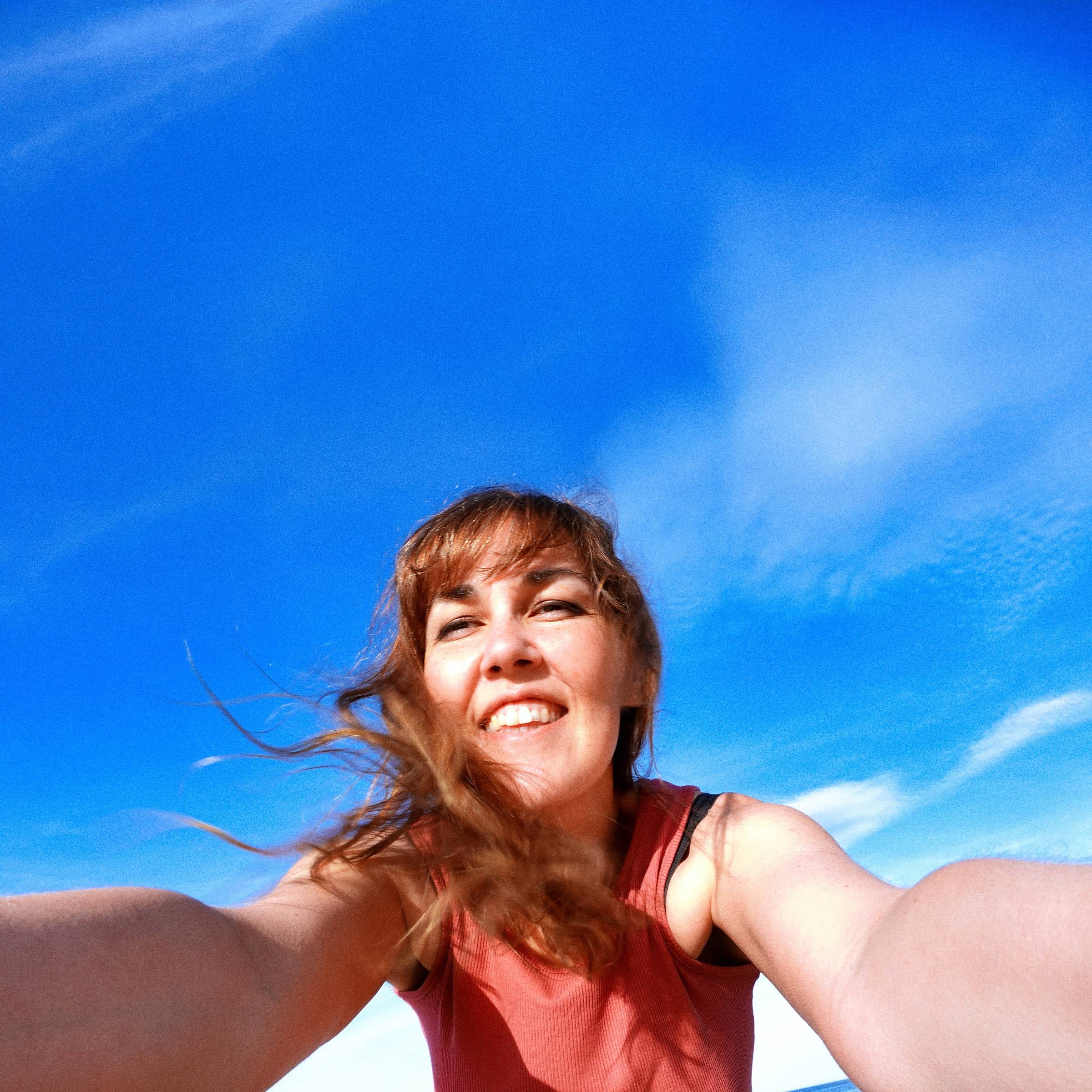 Jay smiling down into the camera with a bright blue sky behind her