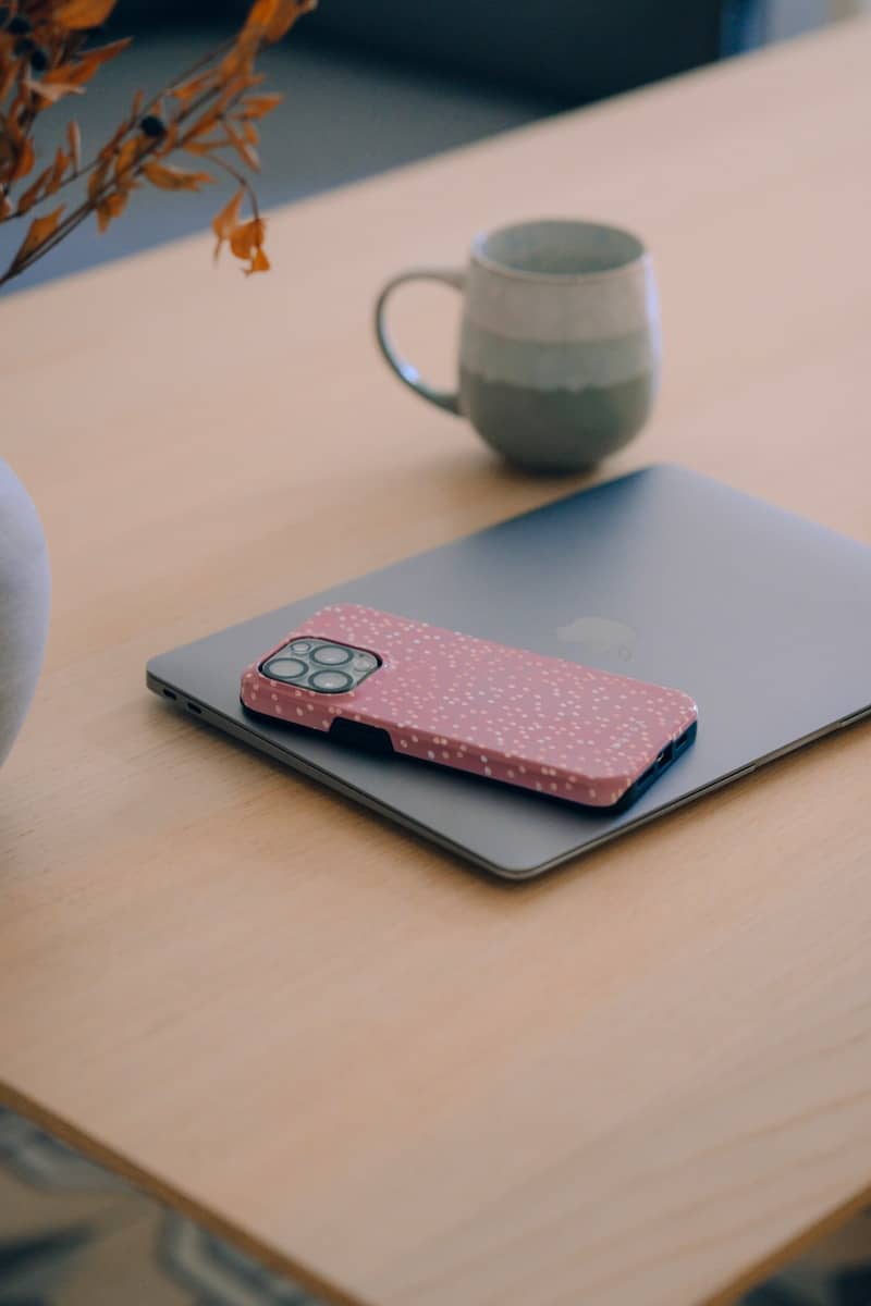 Laptop with pink phone case and mug on table