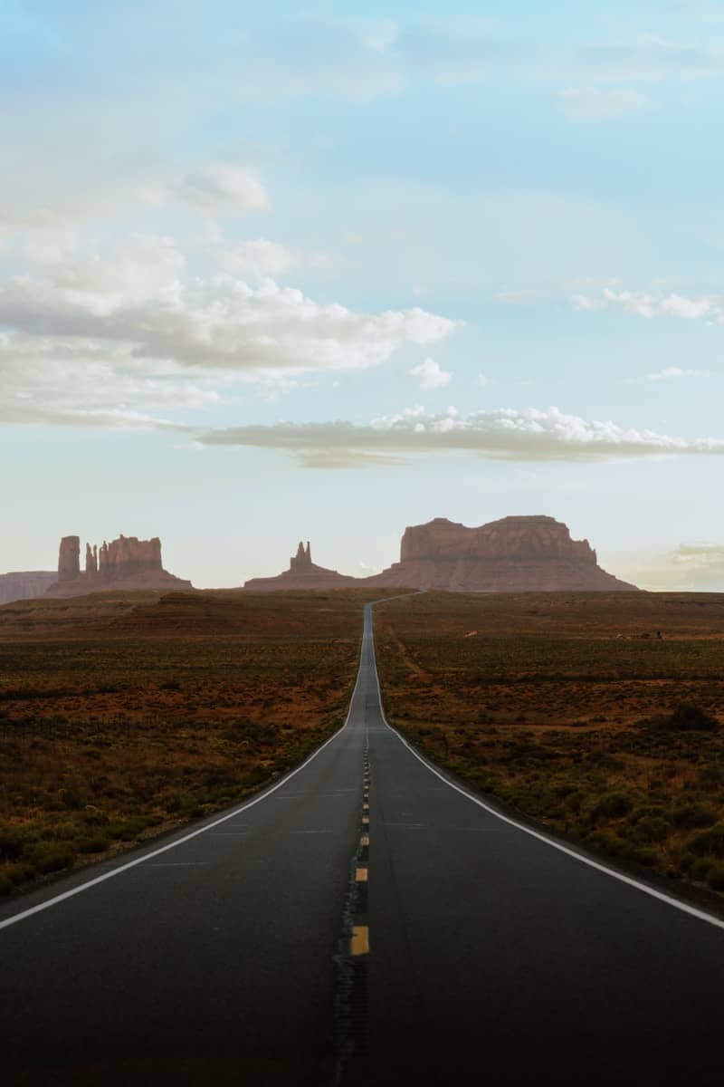 A long, straight road leads to monument valley mesas.