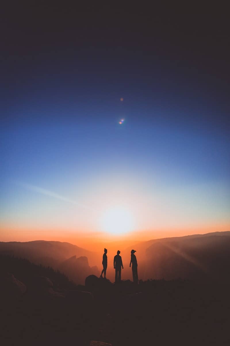 silhouette of three person standing on mountain