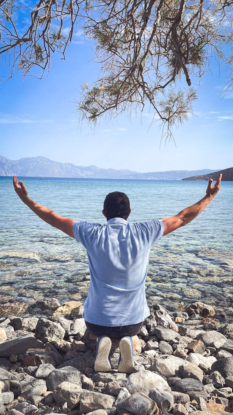 Man kneeling with arms raised towards the sea.